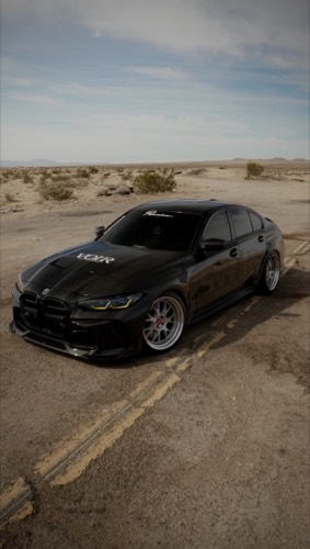 A black BMW M3 with polished wheels parked on an empty desert road under an open sky